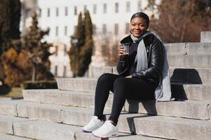 Portrait of a smiling young African American girl with pigtails with coffee walking in the street on a sunny day. Outdoor photo. photo