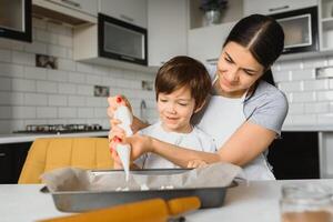 pequeño chico Ayudar su madre con el horneando en el cocina en pie a el mostrador junto a su amasadura el masa para el tarta foto