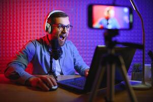 Young man recording or streaming podcast using microphone at his small broadcast studio. Content creator. photo