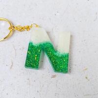 Alphabet letter on white background with gold chain and green sequins. photo