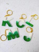 Alphabet letter on white background with gold chain and green sequins. photo