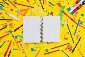 School notebook and stationery over yellow desk. Back to school abstract background. School equipment. Variety of school supplies. Flat lay photo