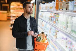 Young man buying groceries at the supermarket. Other customers in background. Consumerism concept. photo