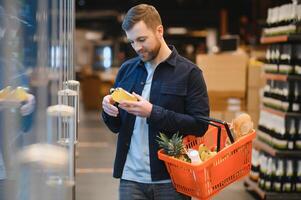 hermoso hombre comprando algunos sano comida y bebida en moderno supermercado o tienda de comestibles almacenar. estilo de vida y consumismo concepto. foto