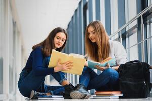 two pretty female students with books sitting on the floor in the university hallway photo