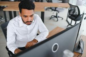 Side view of smart Indian crypto trader, investor, analyst broker, using laptop and smartphone analyzing digital cryptocurrency exchange, stock market charts, thinking of investing and funds risks. photo