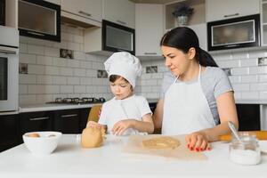 pequeño chico Ayudar su madre con el horneando en el cocina en pie a el mostrador junto a su amasadura el masa para el tarta foto