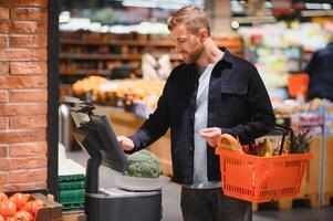 Customer In Supermarket. Man Doing Grocery Shopping Standing With Cart Choosing Food Product Indoors. Guy Buying Groceries In Food Store. Selective Focus, Copy Space. photo