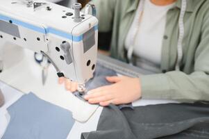 joven modista mujer cose ropa en trabajando mesa. sonriente costurera y su mano cerca arriba en taller. foto
