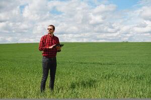 Young agronomist holds tablet touch pad computer in green wheat field. Agribusiness concept. agricultural engineer standing in a wheat field with a tablet in summer photo