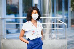 africano americano mujer de negocios vistiendo protector máscara en su cara en el ciudad. el concepto de visitando trabajo durante un pandemia foto