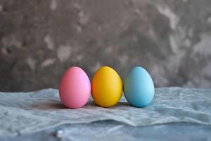 ai generado pastel rosa, amarillo, y azul Pascua de Resurrección huevos alineado en un gris lino superficie, en contra un texturizado fondo con Copiar espacio foto