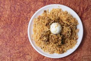 Chicken biryani is a popular Indian dish with egg in the middle. Top view of delicious chicken biryani served on white plate. photo