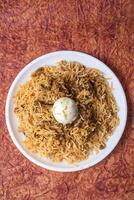 Indian Chicken Biryani dish is delicious and fragrant served on a white plate with egg in the middle, top view. photo