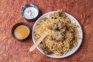 Indian mutton biryani dish served on white plate with raita and gravy. photo