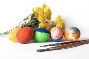 Colorful painted easter eggs with paint brushes and yellow flowers on a white background. photo