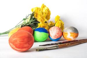 Colorful easter eggs with paint brushes and yellow flowers on a white background. photo