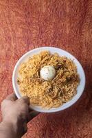 Indian chicken biryani dish served on a white plate with an egg in the middle. Closeup photo