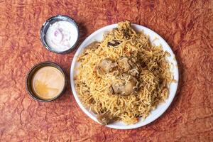 Indian famous mutton biryani dish served on white plate is delicious and fragrant with raita and gravy. photo