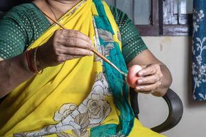 Indian woman holding an easter eggs in her hand and painting it with a paintbrush. photo