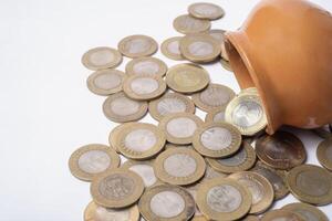 Coins spilling out of an orange ceramic pot on a white background. photo