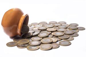 Indian coins falling out of a tilting clay pot are scattered on a white background. Concept of savings and finance. photo