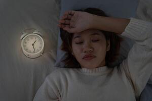 asian woman in bed late trying to sleep suffering insomnia, sleepless or scared in a nightmare, looking sad worried and stressed. Tired and headache or migraine waking up in the middle of the night. photo