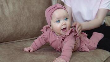 uma bebê menina com loiro cabelo e azul olhos dentro Rosa roupas mentiras em dela barriga e balanços dentro diferente instruções. criança desenvolvimento dentro a primeiro ano do vida video