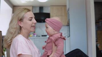 Mother and baby girl with blond hair and blue eyes in pink clothes have fun playing on the background of a modern kitchen set video