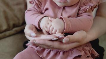 del bambino mani nel La madre di mani. avvicinamento Visualizza di mani. bambino ragazza con blu occhi nel un' carino rosa completo da uomo si siede nel di mamma giro video