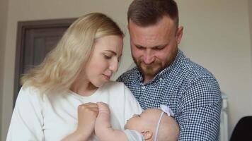 Mother and father hugging and admiring their baby while the child sleeps in the arms of the mother. Fatherhood and motherhood. Traditional family video