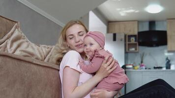 Mother and baby girl with blond hair and blue eyes in pink clothes huddle together against the backdrop of a modern kitchen set video