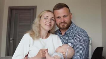 A mother and father hugging, looking at the camera and admiring their baby while the child sleeps in the mother's arms. Fatherhood and motherhood. Traditional family video