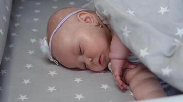 The baby girl sleeps in a cradle with gray bedding and makes a sucking movement with her mouth. The baby dreams of breastfeeding video