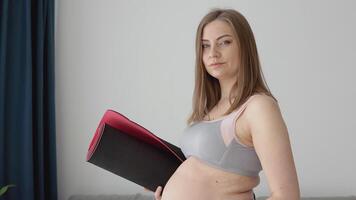 Pregnant woman in sportswear standing with fitness mat in hands at home in living room. Health and sports care during pregnancy. video