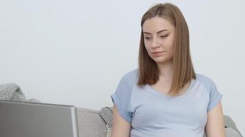 un' incinta donna nel casa Abiti è seduta su un' divano e utilizzando un' il computer portatile. terzo trimestre di gravidanza. preparazione per parto e cura di il neonato bambino video