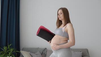 zwanger vrouw in sportkleding staand met geschiktheid mat in handen Bij huis in leven kamer. Gezondheid en sport- zorg gedurende zwangerschap video