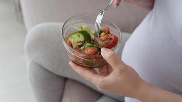 Pregnant woman in home clothes holding a salad of fresh vegetables and a fork. Third trimester of pregnancy. Care for the health of a pregnant woman video