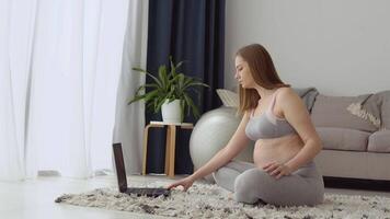 Pregnant woman in sportswear at home in the living room doing exercise for video lessons with a laptop. Health care and sports during pregnancy