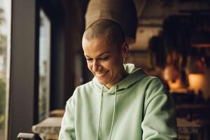 Woman with a bald hair style smiling using a device indoor photo