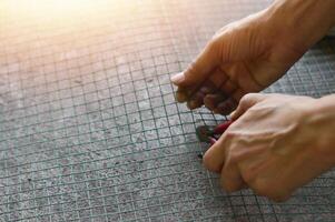 Technician uses pliers to cut green wire mesh photo
