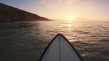 surfer zittend Aan surfboard in oceaan Bij warm zonsondergang. eerste persoon visie van surfing in oceaan video