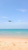 Airplane landing over a white sandy beach and blue ocean in Phuket, Thailand. video