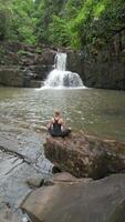 lindo mulher prática meditação às uma cascata dentro a floresta tropical dentro Tailândia video