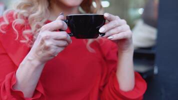 negro taza de café en hembra manos en un rojo antecedentes. al aire libre disparo en el calle video