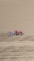 vertical vídeo de rojo tractor trabajando en el campo aéreo ver video