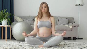 grávida mulher dentro roupa de esporte sentado em a tapete dentro a lótus posição. saúde Cuidado durante gravidez. ioga para grávida mulheres video