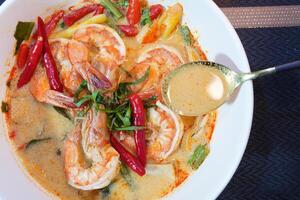 Tom Yam kung Spicy Thai soup with shrimp, seafood, coconut milk and chili in a bowl, close up photo