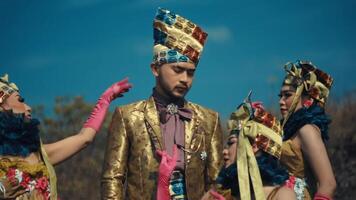 Three models in elaborate traditional costumes with intricate headpieces against a clear blue sky. video