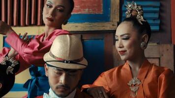 Vintage-styled portrait of three people with a man in a hat at the forefront and two women behind him, against a backdrop of books. video